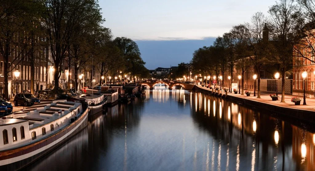 A photo of a city canal at night with boats and buildings illuminated